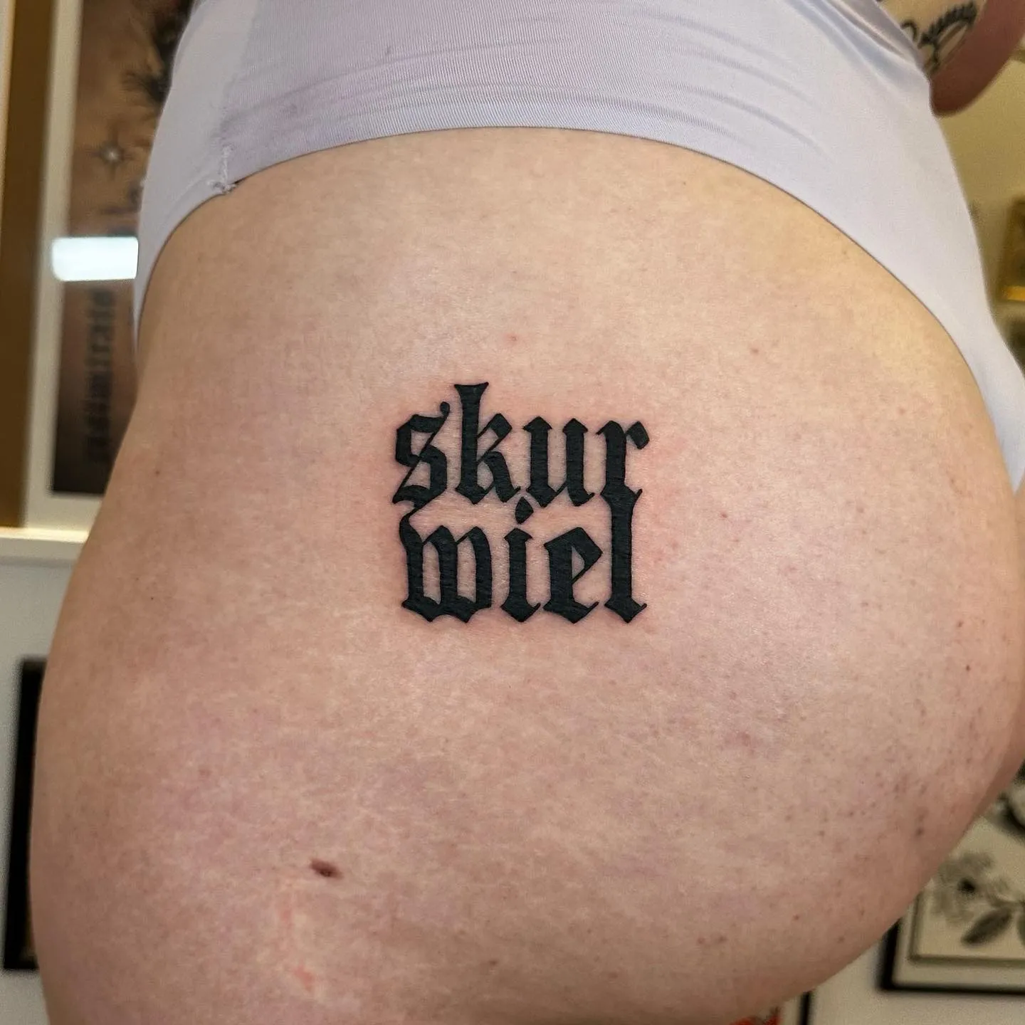 Tatuaż lettering 'Skur Miel' z grubym konturem na ramieniu — tatuaż, Wujek Darek, Warszawa, Polska