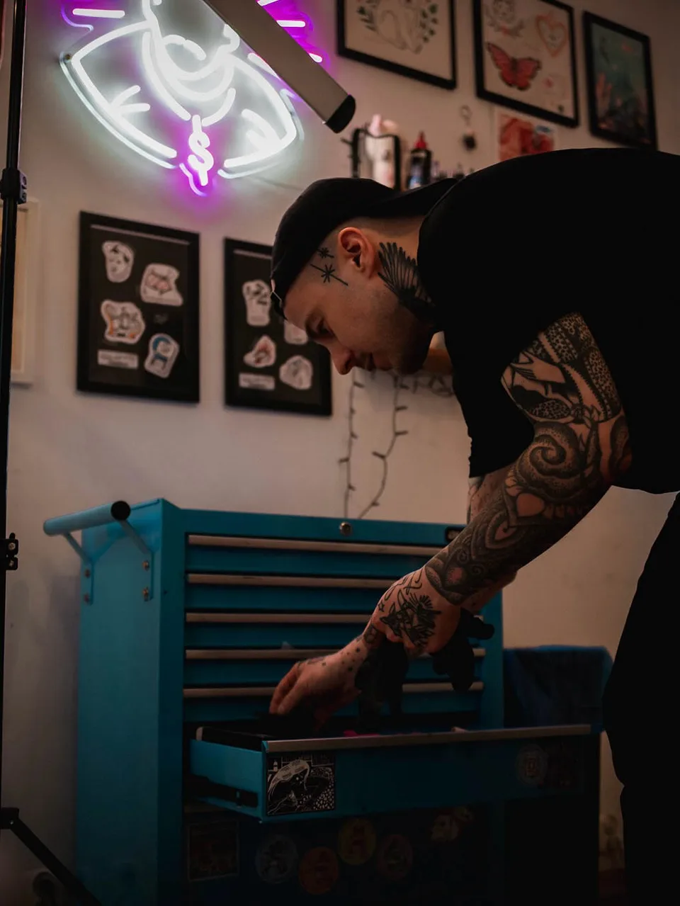 Tatuator z grubo obrysowanym sleeve'em przy niebieskiej szufladzie w studio — Tattoo, Wujek Darek Tattoo, Warszawa