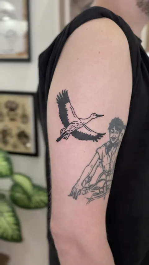 Tatuaż bociana w locie i postać ludzka na ramieniu w stylu ignorant — Tattoo, Wujek Darek Tattoo, Warszawa