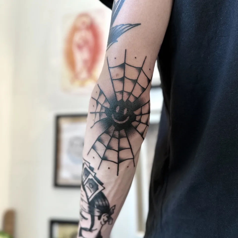 Tatuaż pajęczyny z uśmiechniętą twarzą na łokciu — Tattoo, Wujek Darek Tattoo, Warszawa