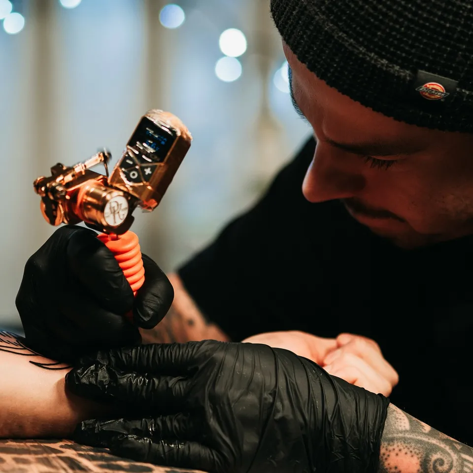 Tatuażysta podczas pracy z miedzianą maszyną rotacyjną — Tattoo, Wujek Darek Tattoo, Warszawa