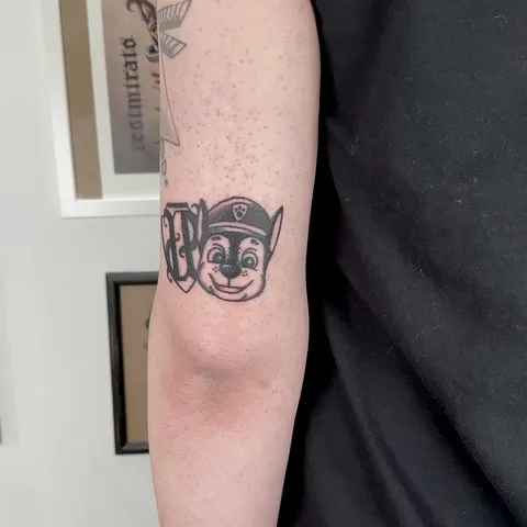 Ignorant tatuaż głowy psa w policyjnej czapce na przedramieniu — Tattoo, Wujek Darek Tattoo, Warszawa