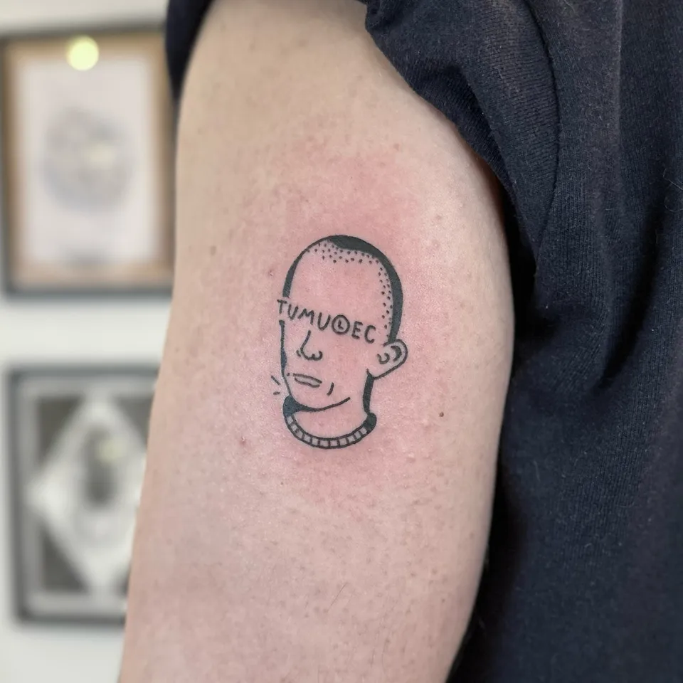 Ignorant tatuaż głowy z napisem na czole i grubym konturem na ramieniu — Tattoo, Wujek Darek Tattoo, Warszawa