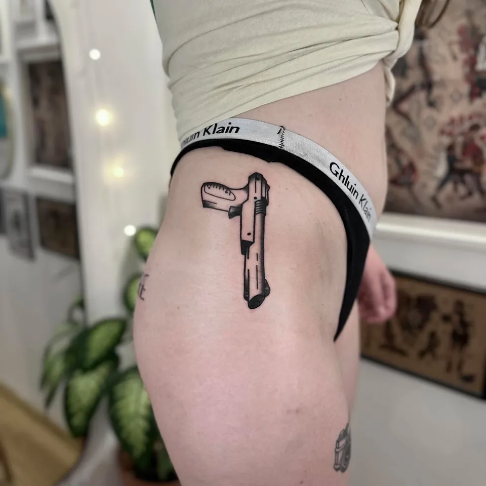 Ignorant tatuaż pistoletu na biodrze z grubym konturem — Tattoo, Wujek Darek Tattoo, Warszawa