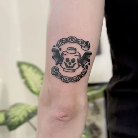 Gruby kontur tatuaż czaszki LEGO z nietoperzymi skrzydłami i łańcuchem — Tattoo, Wujek Darek Tattoo, Warszawa
