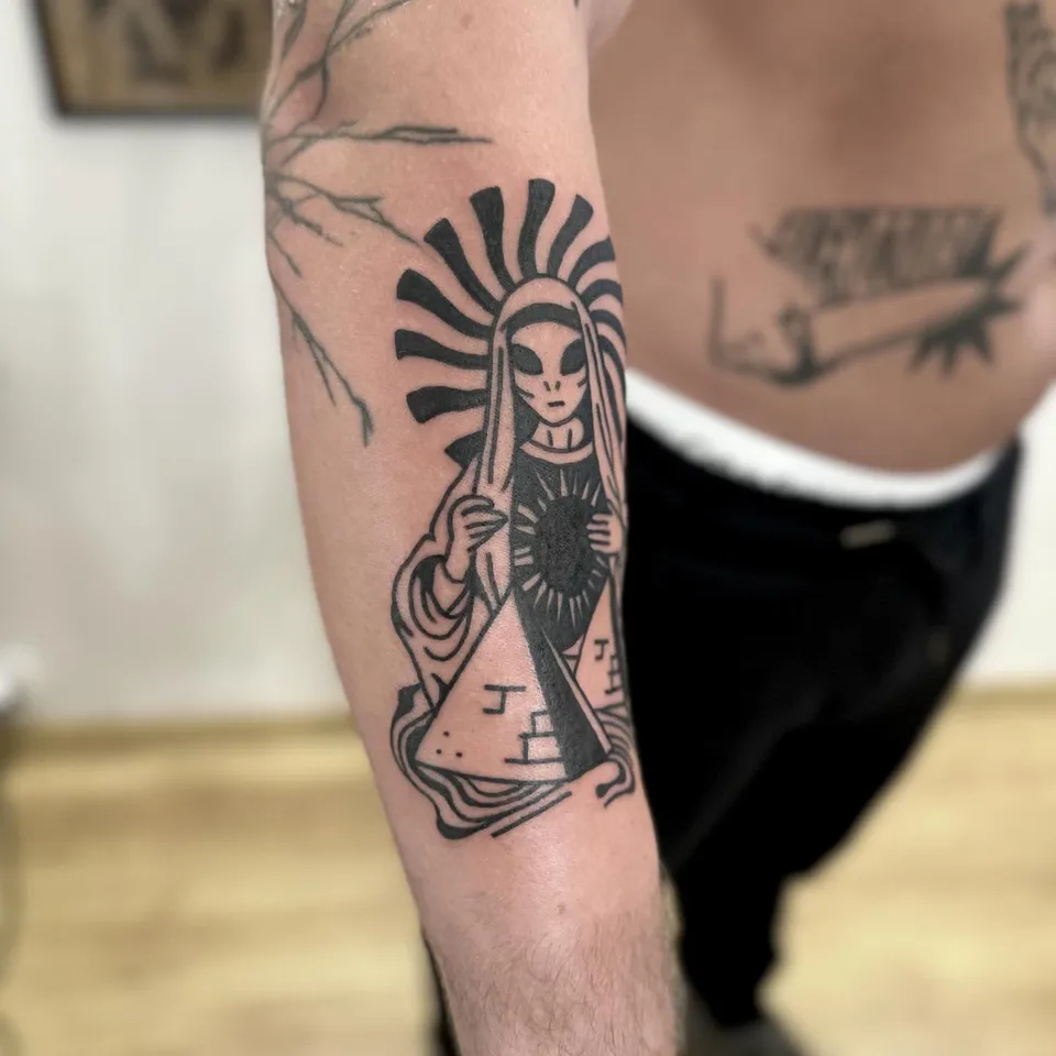 Ignorant tatuaż kosmity w stylu Matki Boskiej z piramidą na przedramieniu — Tattoo, Wujek Darek Tattoo, Warszawa