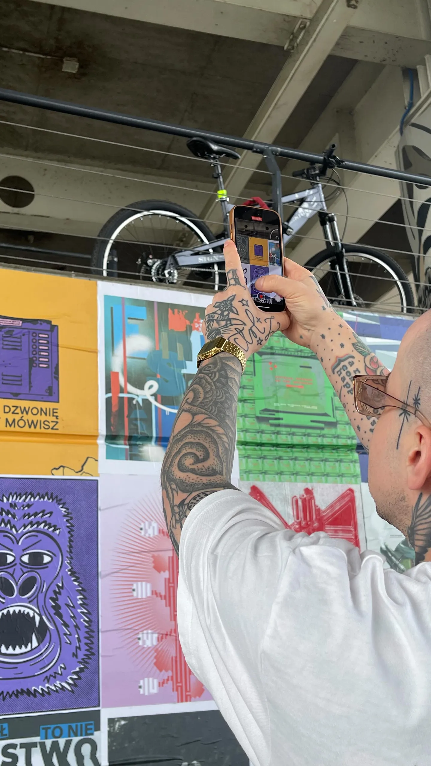 Tatuowany artysta fotografuje plakaty w industrialnej przestrzeni wystawienniczej — Tattoo, Wujek Darek Tattoo, Warszawa