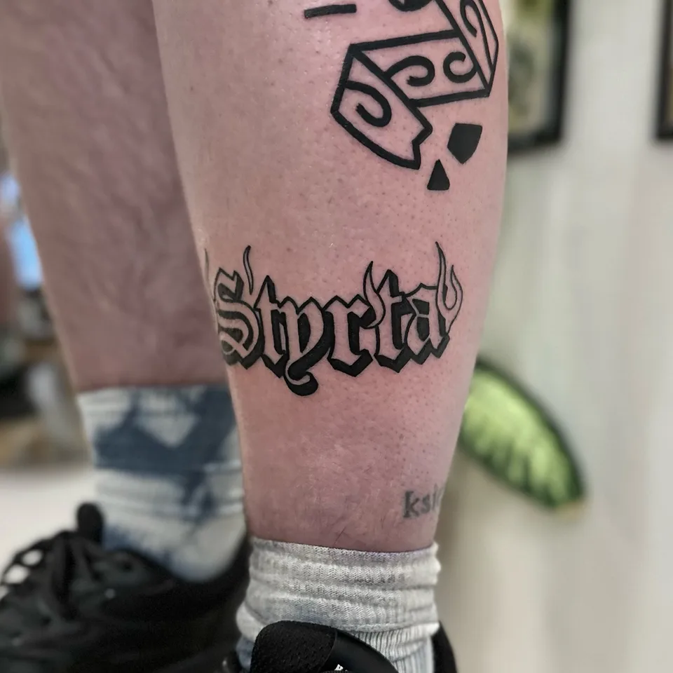 Tatuaż z grubym konturem – słowo w stylu gotyckim z motywem płomieni na łydce (2) — Tattoo, Wujek Darek Tattoo, Warszawa