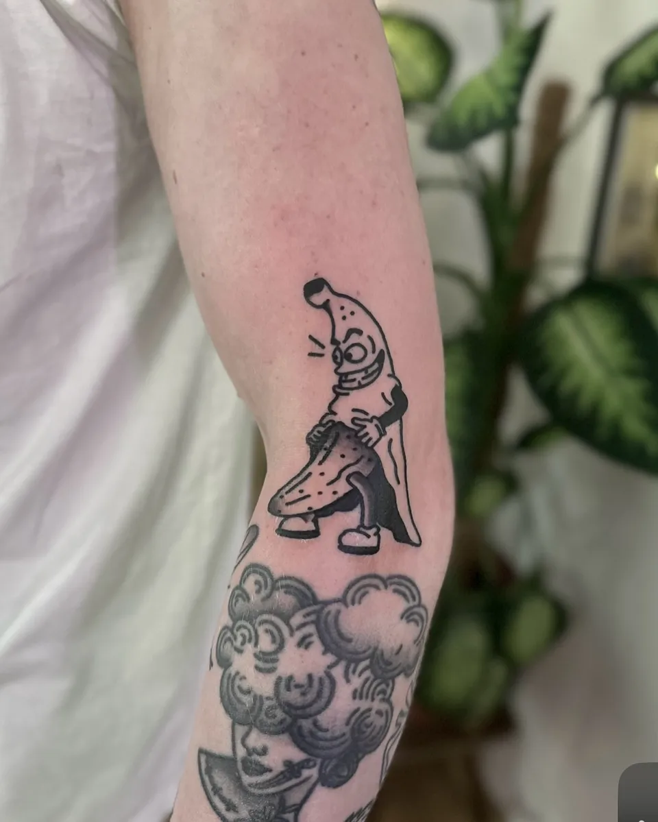 Tatuaż bananowej postaci w stylu ignorant na przedramieniu — Tattoo, Wujek Darek Tattoo, Warszawa