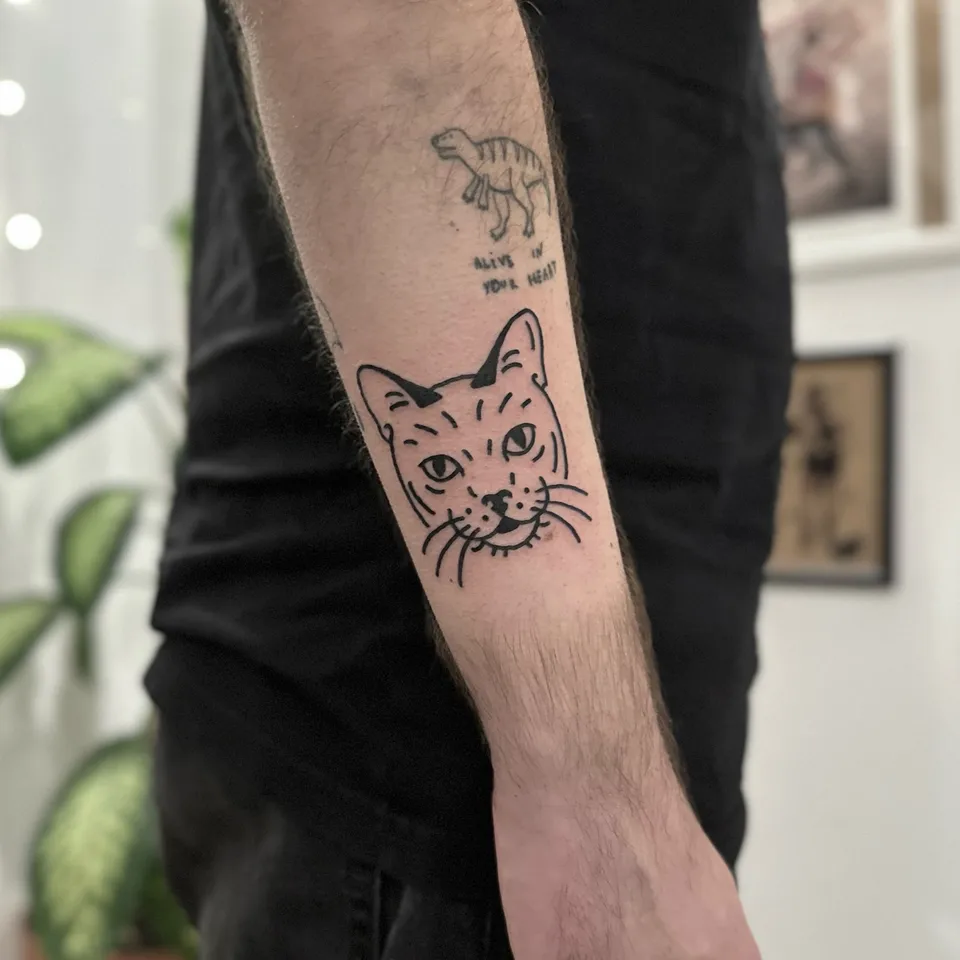 Ignorant tatuaż głowy kota na przedramieniu z grubym konturem — Tattoo, Wujek Darek Tattoo, Warszawa
